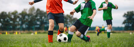 Players kicking football ball on grass. Young boys in a soccer duel. Group of school children playing outoddr sports on soccer pitch. Kids compete in football matchの写真素材