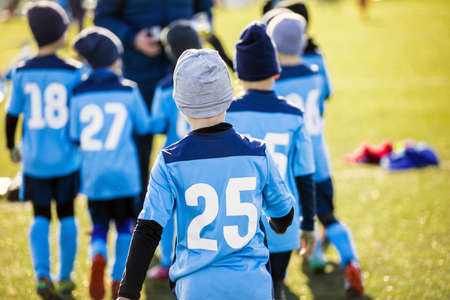 Boys in Blue Soccer Jersey Shirts Following Coach in a Team. Tournament Match for School Kids. Children Playing Sports Outdoor in WInter Sunny Day. Kids in Soccer Winter Clothingの写真素材