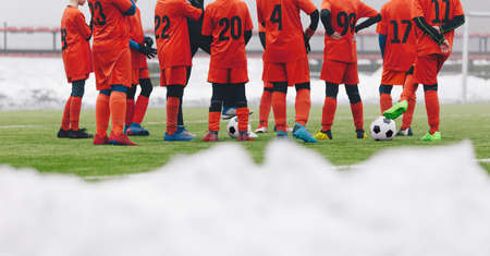 Football Players on Winter Soccer Training Camp. Young Boys Staning in a Circle With Coach on Grass Pitch. Snow Covering Grass Football Fieldの写真素材