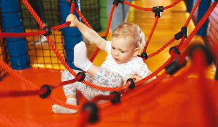Excited little girl playing on net ropes at amusement park. Cute baby girl playing on the colorful...