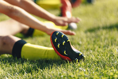Football Player Stretches Sitting on Grass Pitch. Stretching Session After Workout For Footballers. Player in Soccer Cleats and Socksの写真素材