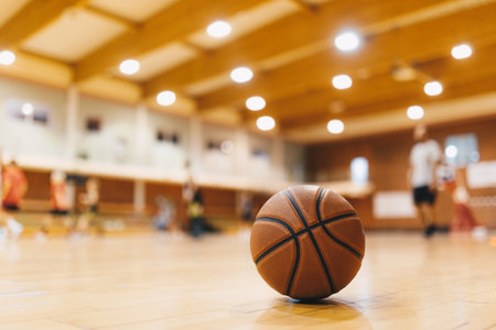 Basketball Training Game Background. Basketball on Wooden Court Floor Close Up with Blurred Players Playing Basketball Game in the Backgroundの写真素材