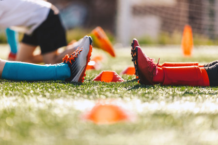 Kids in two sports teams. Legs of two soccer players sit on soccer grass during a training game. Children practicing sports at physical education classの写真素材