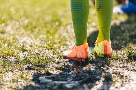 Legs of Soccer Player Standing in Muddy Grass Pitch. Football Clothes Covered With Mud. Junior Level Football Game in Rainy Dayの写真素材