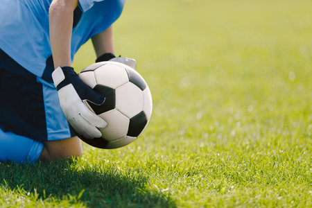 Boy as a football goalie holding the ball in hands ready to start a game. Football goalkeeper play a football match in jersey shirt and soccer glovesの写真素材