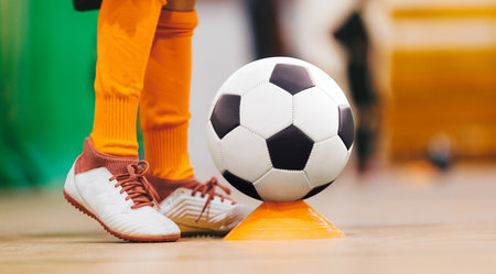 School boy on indoor soccer football training. Soccer ball and orange training cone. Child in sportswear kicking ball on physical education classの写真素材