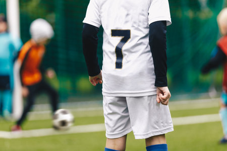 A young boy in a soccer team wearing a white jersey shirt with the number seven on its back. Youth football players playing tournament matchの写真素材