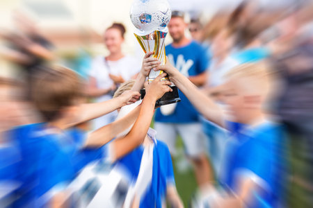 Young Soccer Players Holding Trophy. Young Sport Team with Trophy. Boys Celebrating Sports Achievement. Celebrating Soccer Football Championship. Winning team of sport tournament for kids children.の写真素材