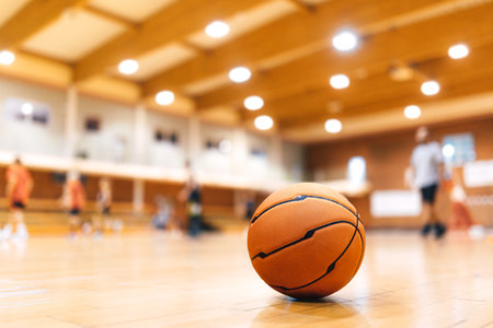 Basketball Ball on Wooden Court. Basketball Game in the Blurred Background. Basketball Court Background. Classic Sports Basketball Ballの写真素材