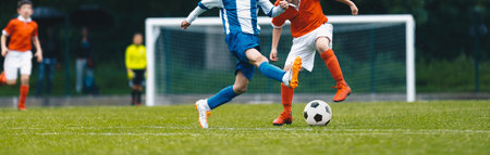 European soccer match between youth teams. Young school boys playing soccer game. Junior competition between players running and kicking soccer ball. Tournament game between red and blue kids' teamsの写真素材