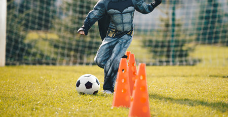 Child in Halloween Costume in Soccer Training. Kids Playing Football Ball on Grass Field. Happy School Boys Kicking Ball During Practice Game. Halloween Football Trainingの写真素材