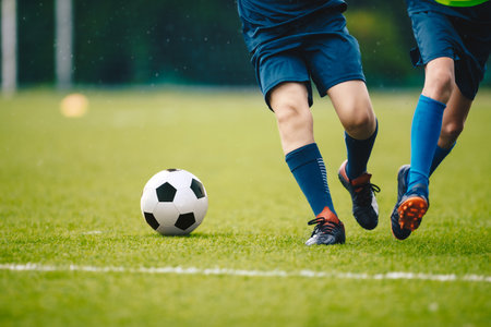 Two adult football players running and kicking a soccer ball. Legs of two young football players on a match. European football youth player legs in actionの写真素材