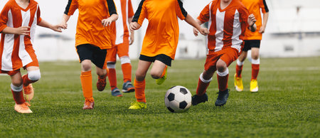 Cchildren having fun in soccer football game. Group of school kids running ball in football duel. School boys in sports outdoor competition. Children in red and orange soccer uniformsの写真素材