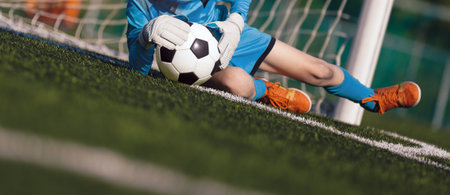 Young boy as a soccer goalie catching the ball during a soccer match. Football goalkeeper in jersey shirt and sports gloves play a football tournament gameの写真素材