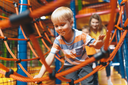 Happy children playing together with a nanny at an amusement park. Excited kids playing together on net ropes. Cute school kids playing on the colorful playground at a shopping mallの写真素材