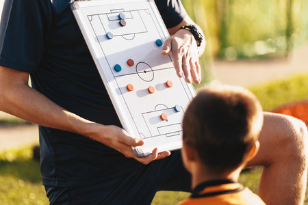 Football Coach Using Soccer Tactics Strategy Board. Coach explaining the game plan to school soccer players. Kids at physical education trainingの写真素材
