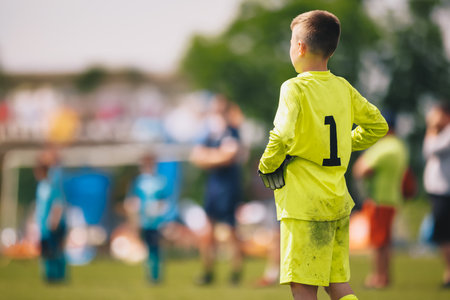 Young Soccer Goalie On The Pitch. Young Boy Soccer Goalkeeper. Soccer Game on Sunny Summer Day. Sports Activities for Children. Football Match in the Background. Youth Sports Wallpaperの写真素材