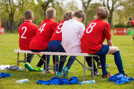 Kids in the Sports Team on Substitute Bench. Young Football Players. Young Soccer Team Sitting on Bench. Soccer Match For Children. Young Boys Playing Tournament Soccer Match. Youth Soccer Clubの写真素材