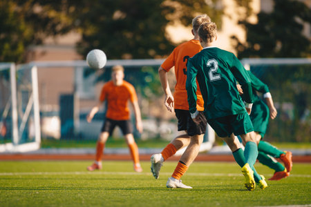 Soccer football players kick a ball towards a goal during a match in the soccer stadium. Youth football teams in a game. Footballers in action on the tournament game. Adult football competitionの写真素材