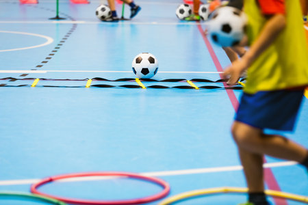 Indoor soccer training class for children. Physical education class for school kids. Children improving agility. Soccer skills training. Futsal players in practice game at sports hallの写真素材