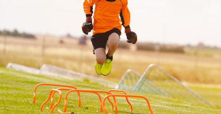 Young Soccer Goals in Training Action. Boy Soccer Player Improving Speed Skills. Kid Goalkeeper in a Practice Session. Footballer Running And Jumping Over Hurdlesの写真素材