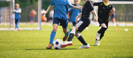 Happy kids compete in football game. Young boys playing soccer game. Kids having fun in sports. Running soccer players. Competition between players running and kicking football ball. Football schoolの写真素材