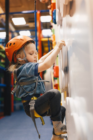 Happy Boy in Helmet on Climbing Class at Indoor Climbing and Bouldering Center. Kid Boy Smiling to the Camera and Keeping Thumb Upの写真素材