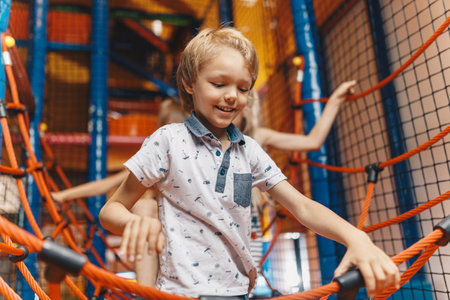Happy group of siblings playing together on indoor playground. Excited kids playing together on net ropes. Cute school kids playing on the colorful playground at shopping mallの写真素材
