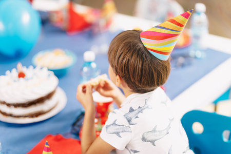 Child at Birthday Party. Anonymous Birthday Boy Wearing Birthday Cap and Having Fun During Children Party. School Boy Sitting at Birthday Tableの写真素材