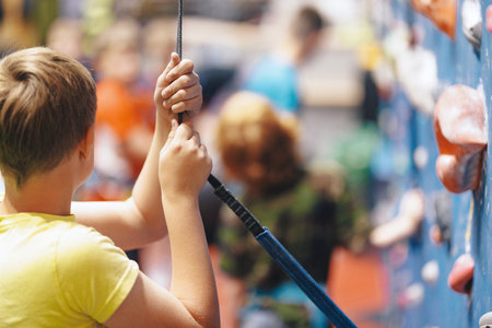 Happy boy hanging on climbing rope and climbing up in bouldering climbing center. School kids playing on the climbing wallの写真素材