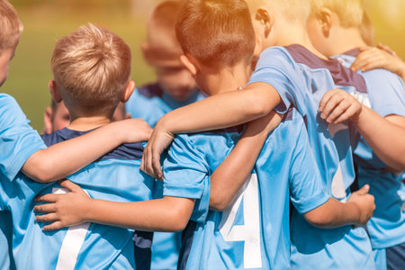 Happy boys united in a sports team. Group of kids in blue jersey t-shirts huddling together at the sports venue. School kids have fun and building team spirit during sports competitionsの写真素材