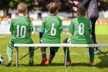 Young Soccer Players Wearing Jersey Green Shirts and Sitting on Bench Before Match at Stadium. Kids Play Game in Youth Soccer Football Leagueの写真素材