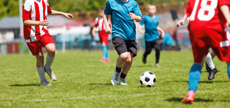 Youth Soccer Match in Action: Kids Competing on Grass Field in Colorful Uniforms During Sunny Dayの写真素材