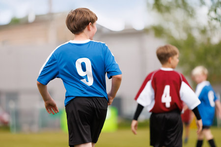 Kids in Blue and Red Jerseys on Soccer Field. Youth Soccer Match in Action. Kids Competing on the Field Wearing Blue and Red Team Jerseys during Football Practiceの写真素材