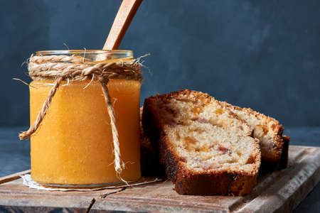 jam accompanied with bread with fruits on a wooden board with a spoon on a blue background