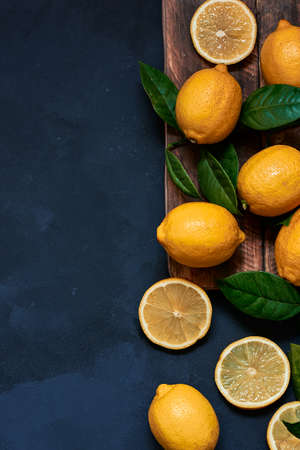whole and sliced lemons on a wooden board with leaves on a dark blue background