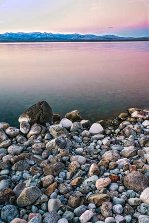 stony shoreline over a lake at sunset with mountains in the backgroundの写真素材