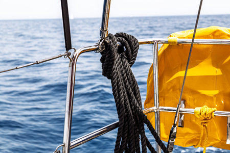 A close-up view of a yacht railing with a black rope looped around a metal fitting and a yellow...