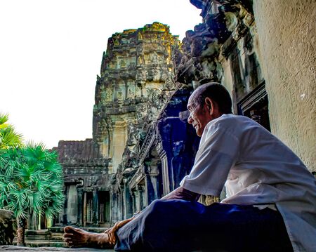 Angkor Wat, Siem Reap, Cambodia. August 20, 2009: The ruins of Angkor Thom, the capital of the Khmer Empire, the ancient temple of Bayon. Elderly man in a white shirt is sitting resting looking forwardのeditorial素材