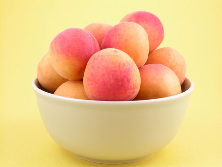 bowl full of fresh and sweet apricots on yellow background close-upsの写真素材