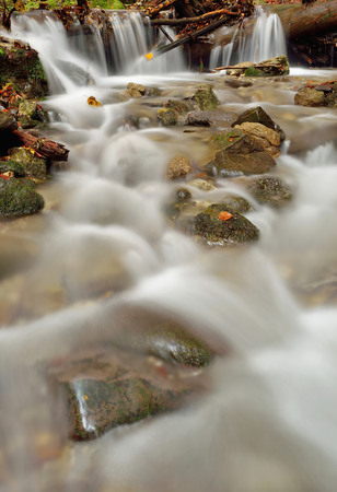 Autumn flowing mountain stream waterfall in Slovakia. Colored leafs on moss rock. Fresh natural water.の写真素材