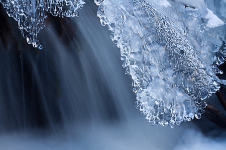 Water and ice in winter mountain stream. Cold icing shapes.
