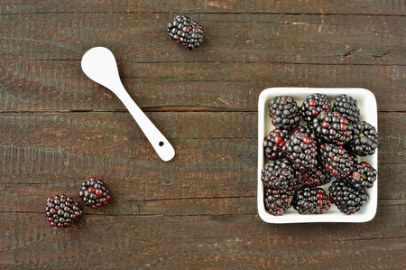 Blackberry fruit on wood background. Forest fruit in white idaeus and spoon. Delicious fresh berries.の写真素材