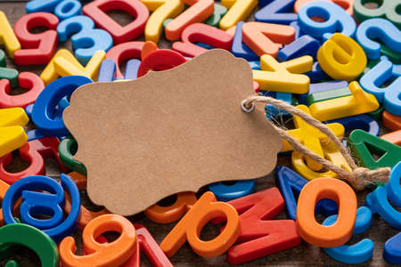 Blank craft brown paper tag with colorful plastic alphabet on wooden background