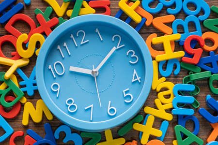 Blue alarm clock with colorful alphabet and numbers on wooden backgroundの写真素材