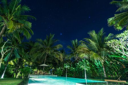 swimming pool with palm trees at night. beautiful sky with starsの写真素材