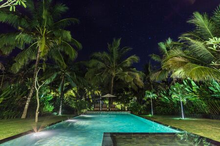 illuminated swimming pool at night in a tropical gardenの写真素材