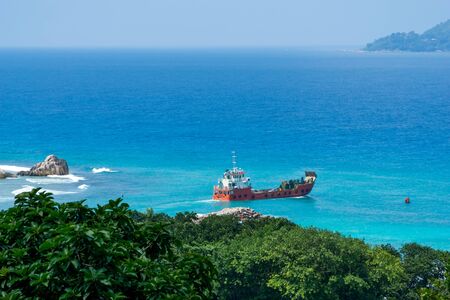 Panoramic view of famous granite rocks in blue sea at La Digue, Seychelles. orange cargo ship going...