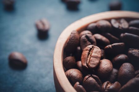 extreme close-up of a wooden bowl filled with roasted coffee bean on a dark slate background. horizontal format with copy space for textの写真素材