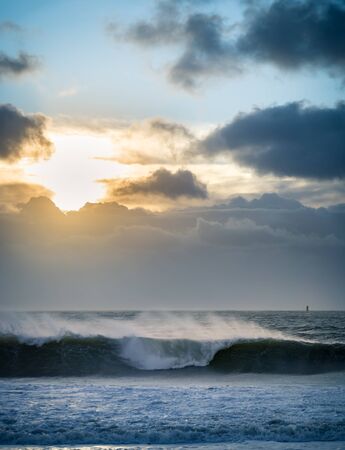 Sunrise over the sea during a storm. Dramatic clouds and rays of the sun illuminate ocean spray .の写真素材